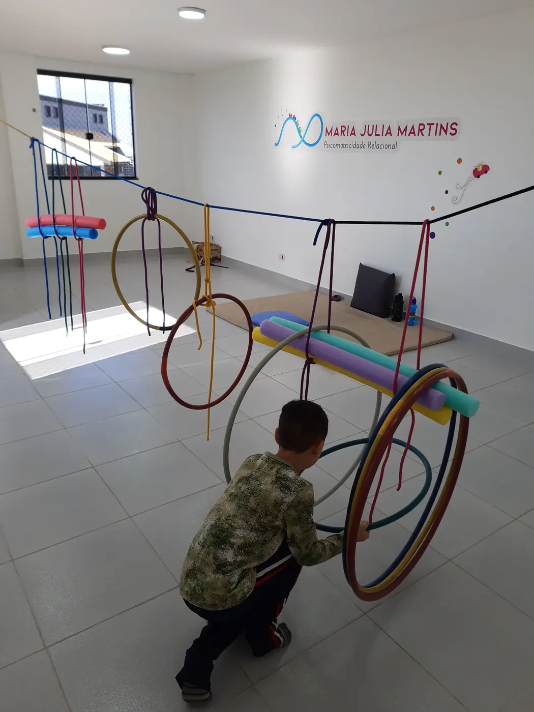 Criança brincando em um circuito montado com bambolês e bastões coloridos no salão de atendimento