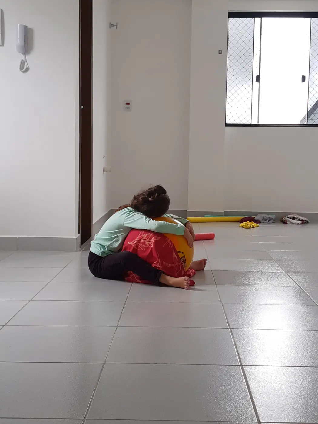 Criança sentada no chão, abraçada a uma bola colorida durante a sessão