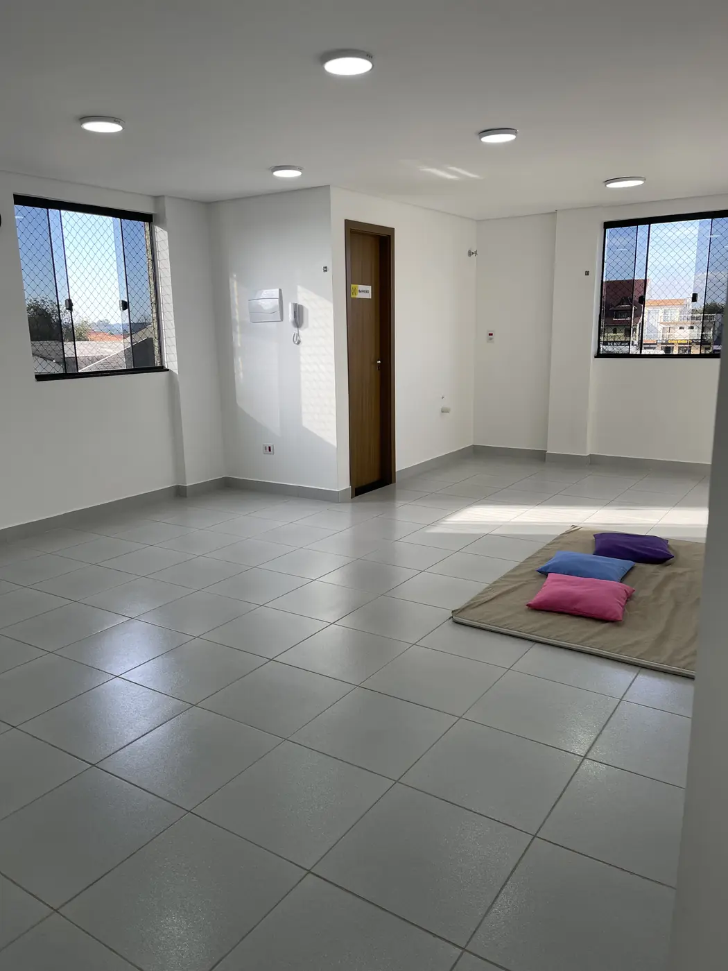 Salão de atendimento amplo e claro, com luz natural pelas janelas e almofadas sobre um tapete